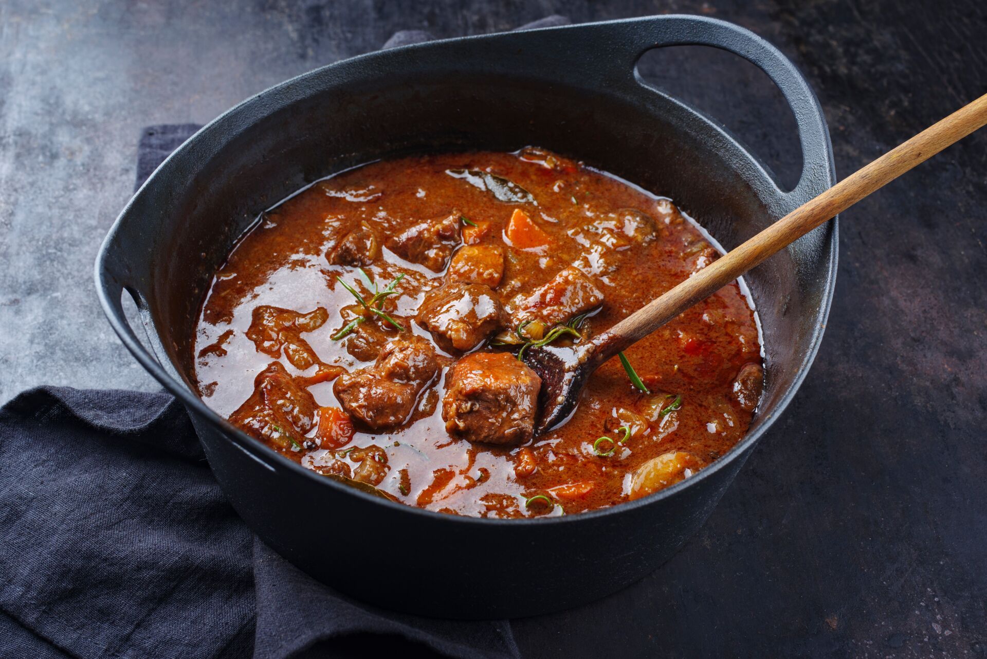 Ein Topf, wo Rindergulasch drin ist und mit einem Kochlöffel umgerührt wird