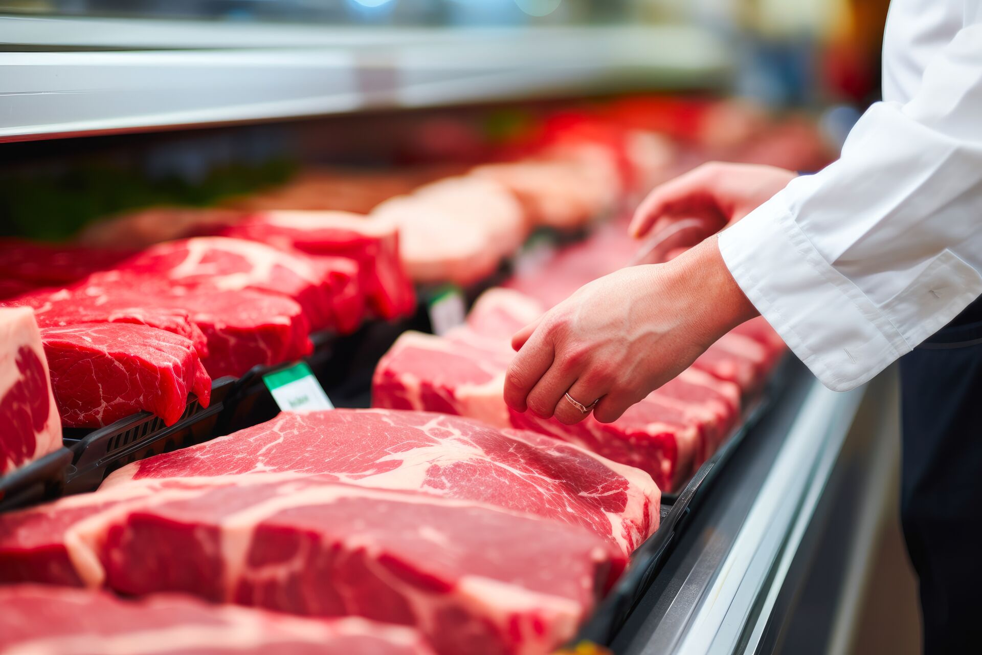 Eine Person in Arbeitskleidung präsentiert eine Auswahl an rohem Fleisch