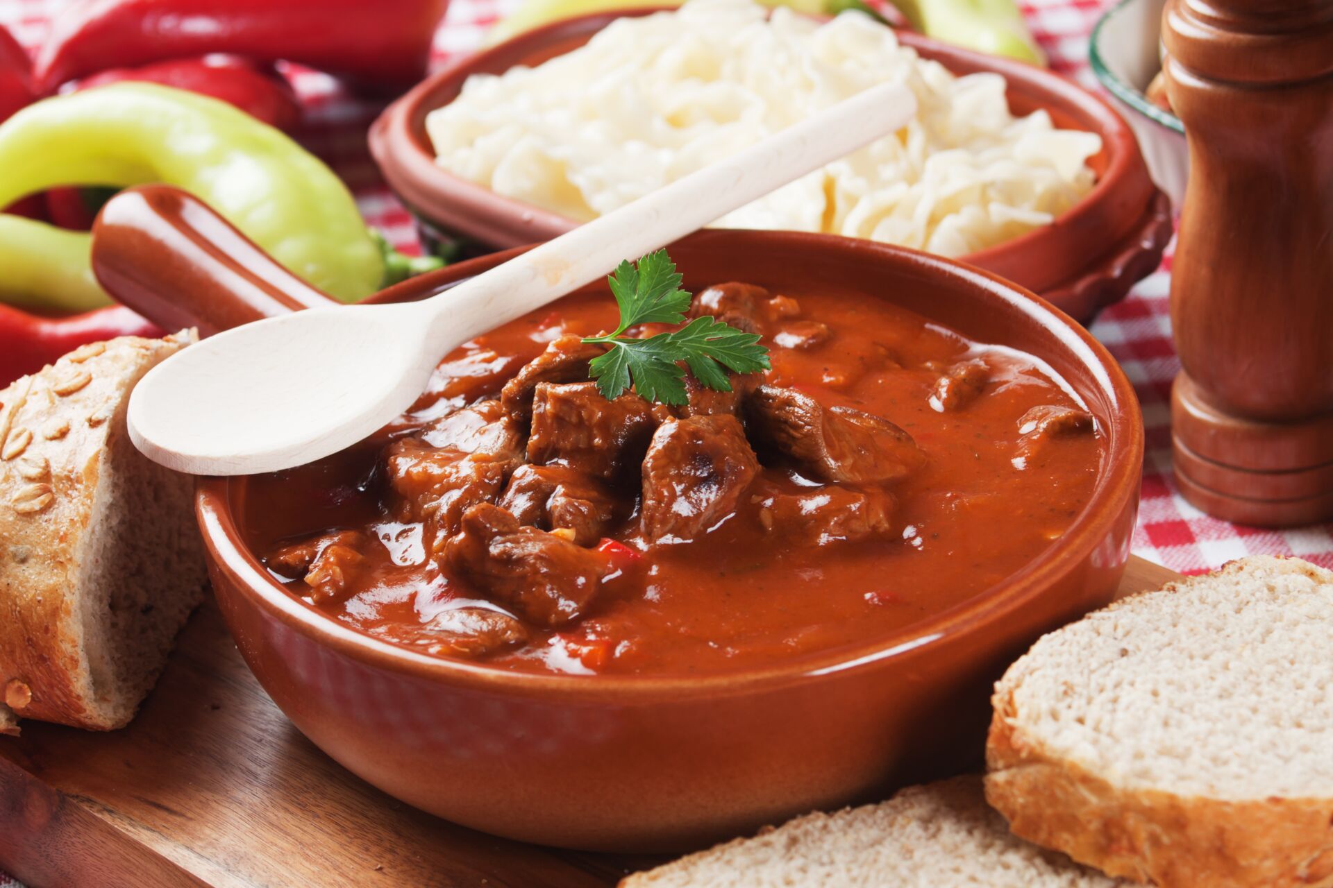 Eine Schüssel, wo Rindergulasch drin ist und neben der Schüssel liegt brot und Paprika